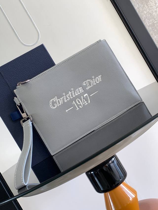 这款 A5 手拿包是一款优雅简约的配饰。采用迪奥灰粒面牛皮革精心制作，饰以“Christian Dior 1947”标志刺绣，向 Dior 承传致敬。拉链隔层内
